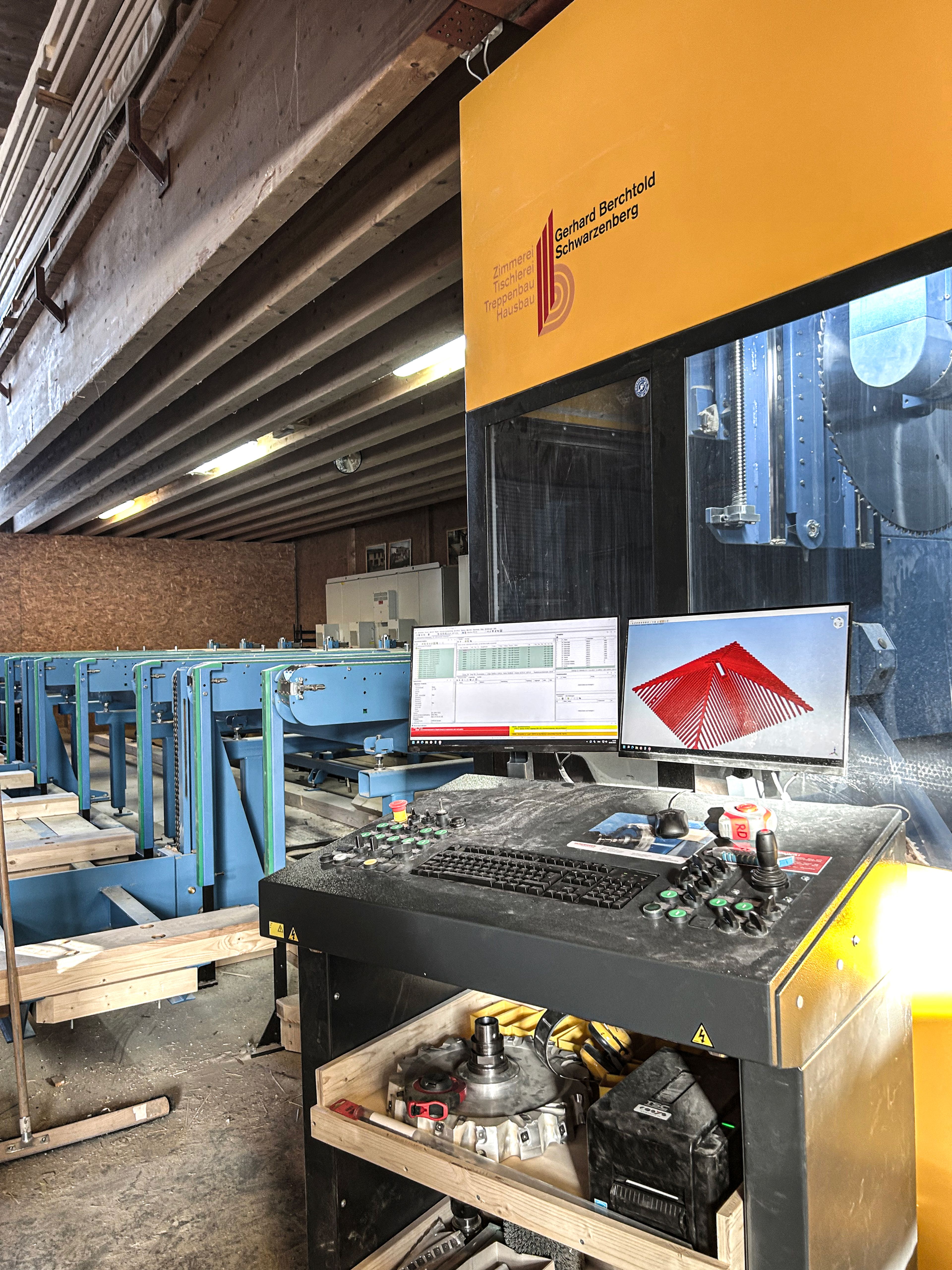 Industrielles Maschinenbedienfeld mit mehreren Bildschirmen, Knöpfen und Drehreglern in einer Fabrikumgebung, im Hintergrund blaue Maschinen.