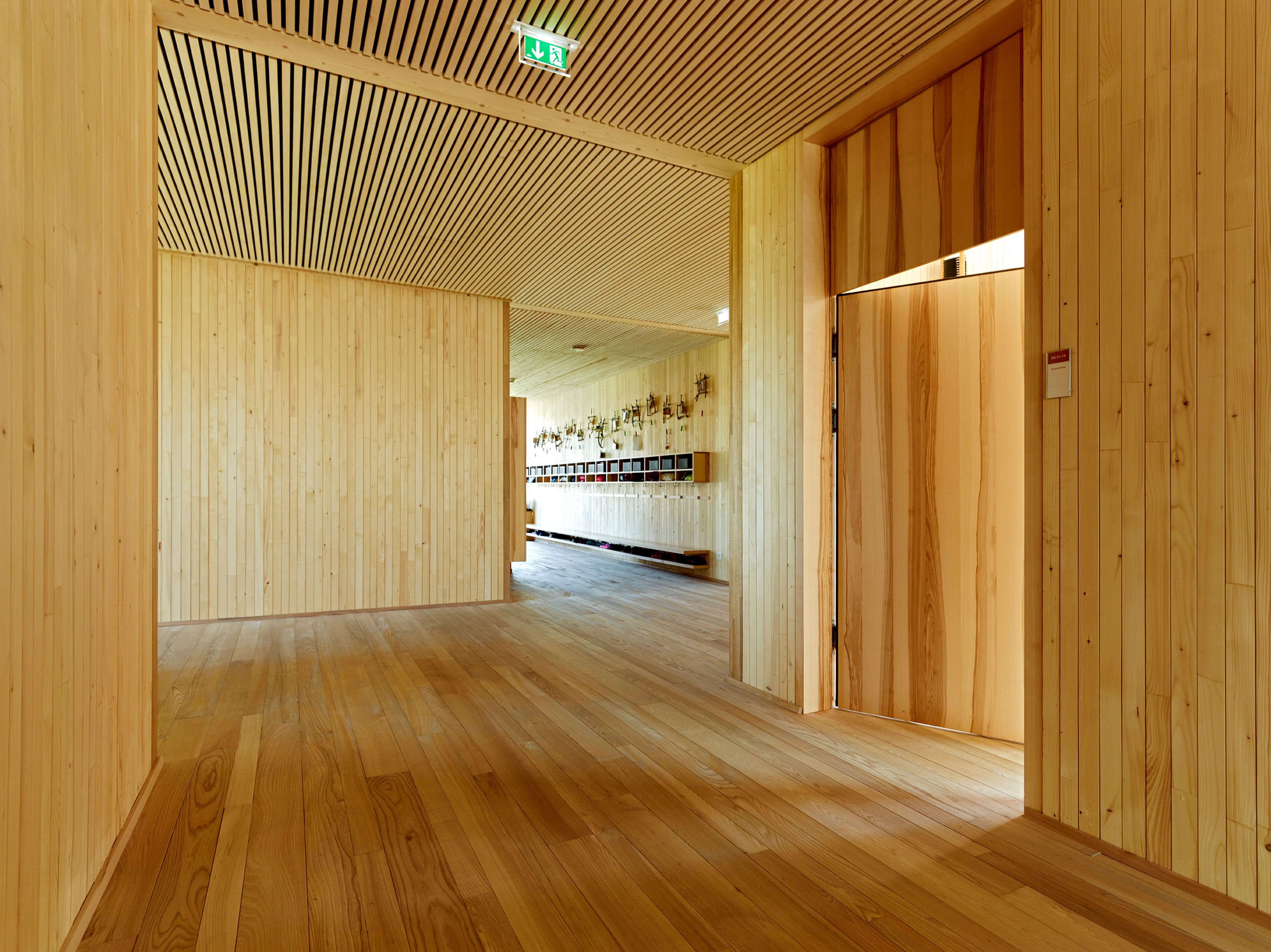 Innenraum eines Kindergartens mit durchgehendem Holzboden, Holzdecken und Holzwänden in heller, freundlicher Gestaltung. Die natürliche Materialität schafft ein gesundes Raumklima und eine warme, behagliche Umgebung. Lichtdurchflutete Räume mit klarer Struktur und kindgerechter Ausstattung laden zum Spielen, Lernen und Wohlfühlen ein. Die nachhaltige Holzbauweise vermittelt Sicherheit, Natürlichkeit und eine perfekte Umgebung für Kinder.