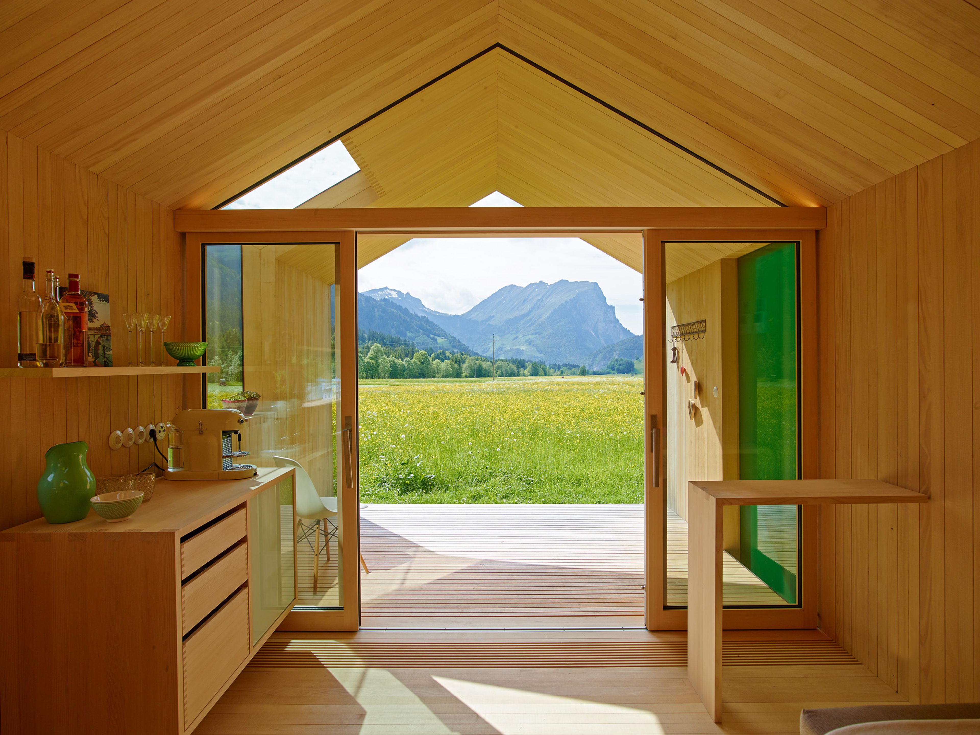 Kleines, modernes Gartenhaus in Holzbauweise mit Schindelfassade, klarer Formensprache und großem Fenster, umgeben von Grün.