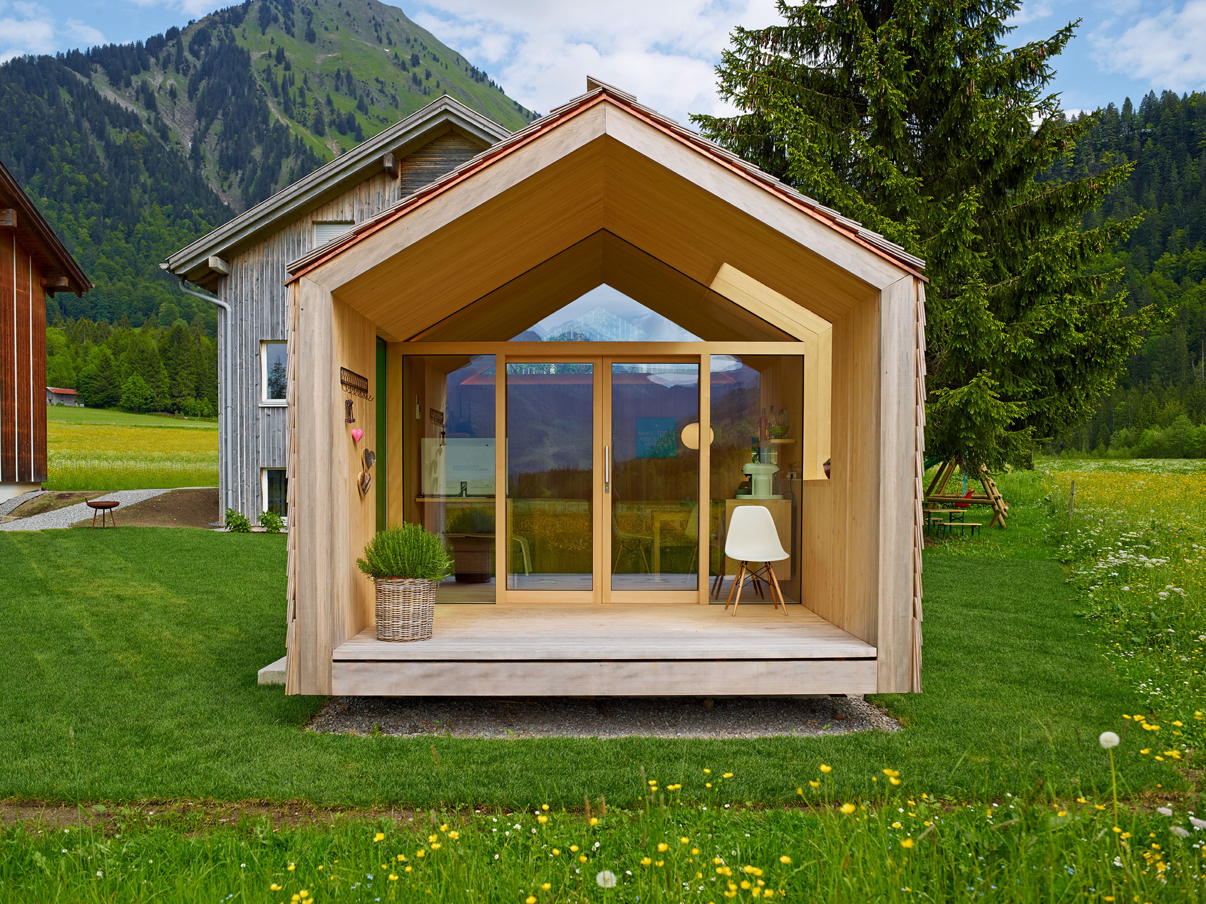 Kleines, modernes Gartenhaus in Holzbauweise mit Schindelfassade, klarer Formensprache und großem Fenster, umgeben von Grün.