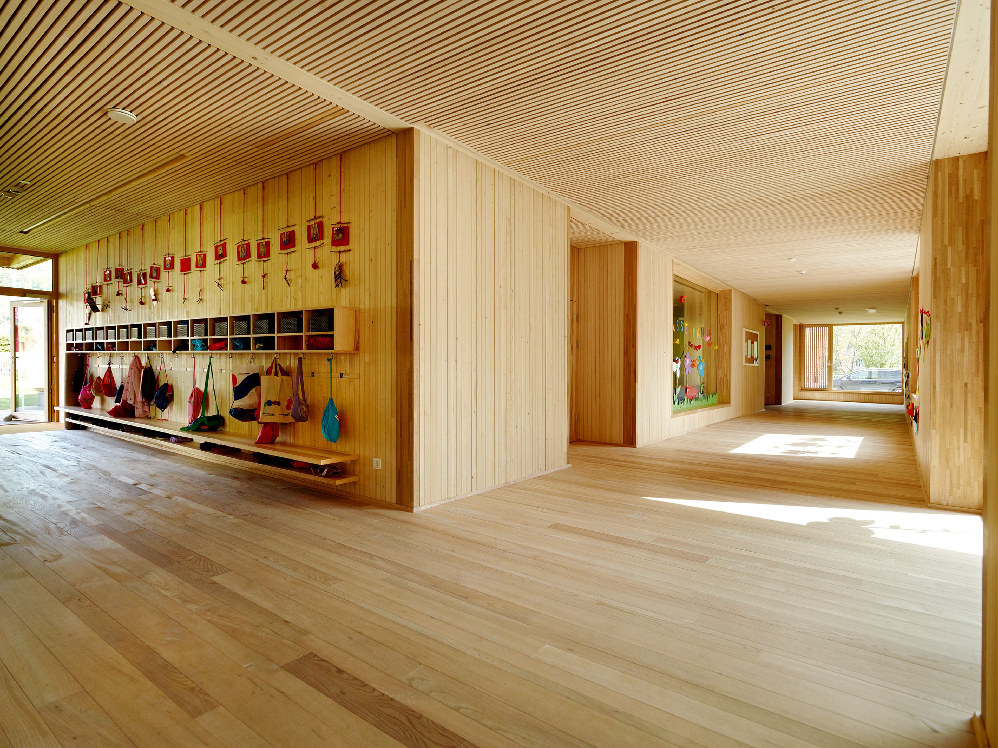 Innenraum eines Kindergartens mit durchgehendem Holzboden, Holzdecken und Holzwänden in heller, freundlicher Gestaltung. Die natürliche Materialität schafft ein gesundes Raumklima und eine warme, behagliche Umgebung. Lichtdurchflutete Räume mit klarer Struktur und kindgerechter Ausstattung laden zum Spielen, Lernen und Wohlfühlen ein. Die nachhaltige Holzbauweise vermittelt Sicherheit, Natürlichkeit und eine perfekte Umgebung für Kinder.