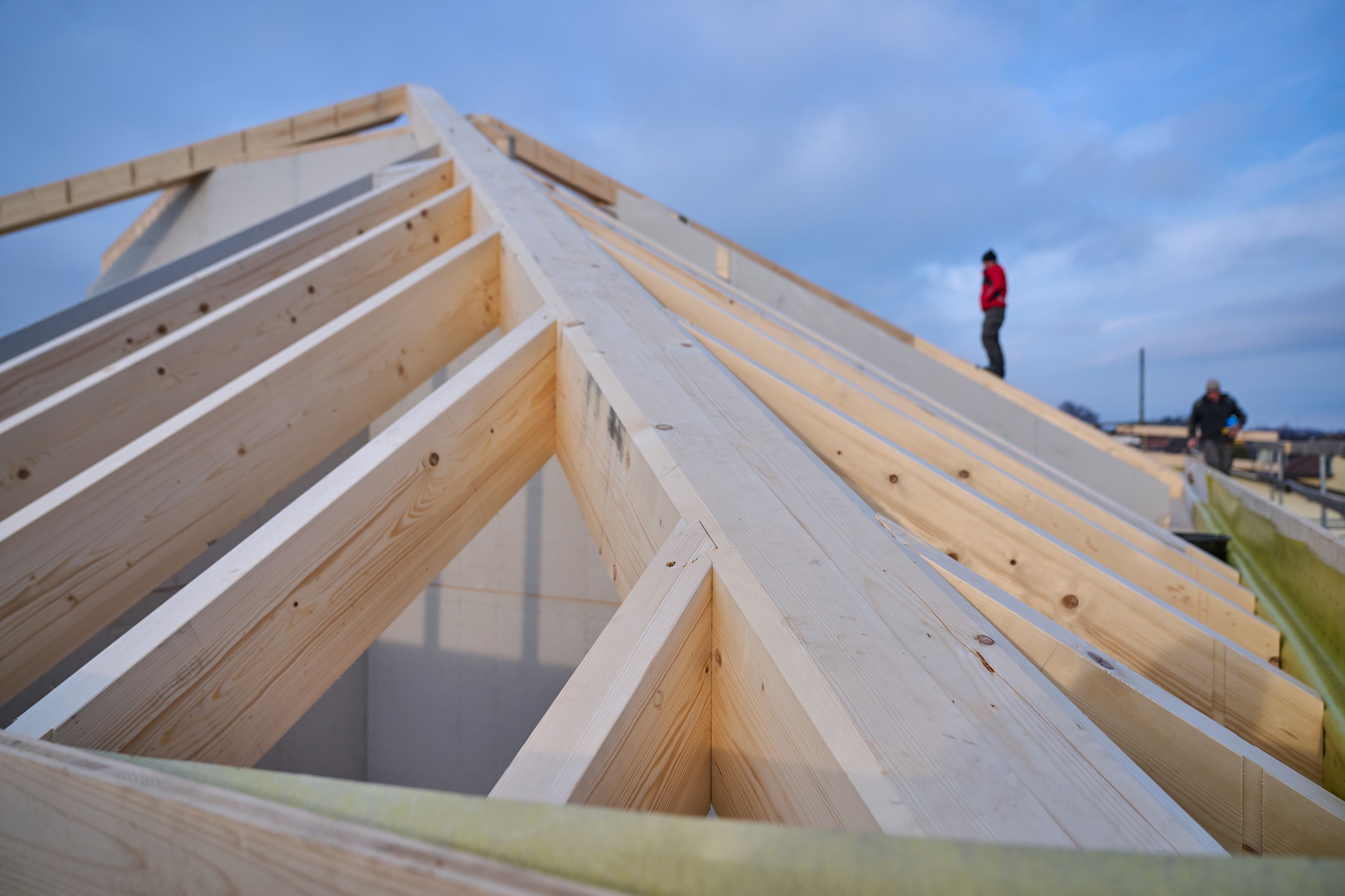 Zimmerer auf der Baustelle, im Vordergrund ein Dachstuhl in Holz