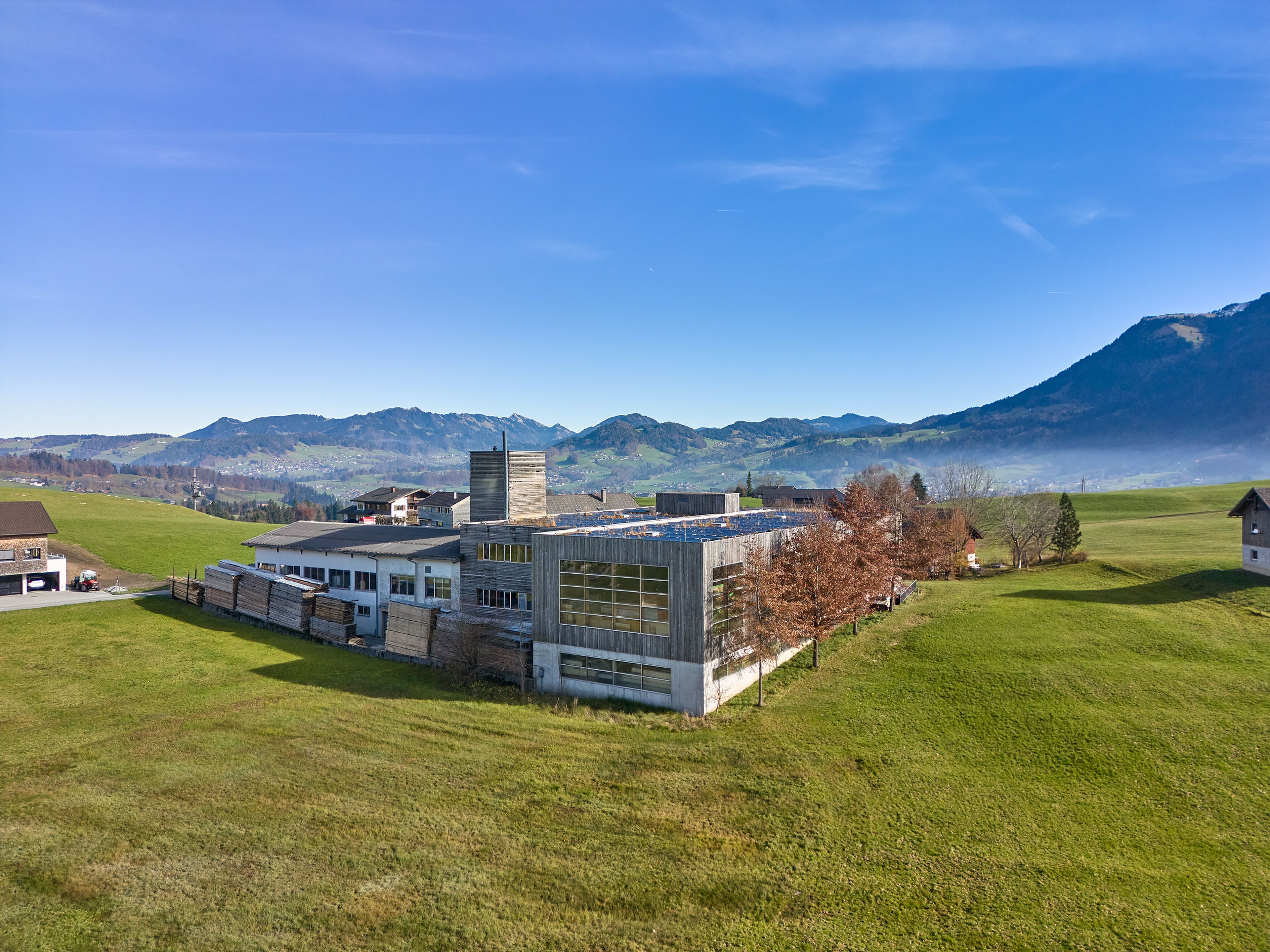 Modern building in a grassy rural landscape with mountains in the background under a clear blue sky.