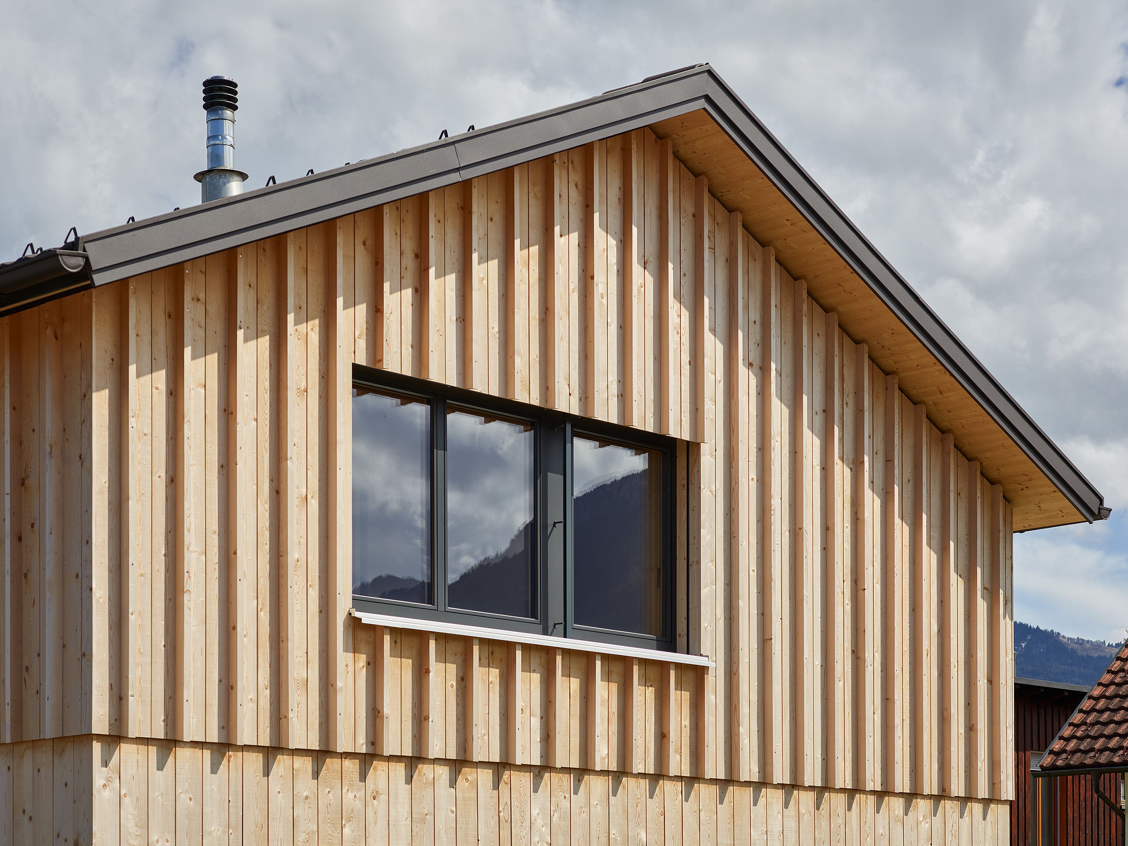 Außenansicht und Detail Fassade eines Holzhauses in gestrickter Bauweise mit vertikaler, stehender Holzfassade.