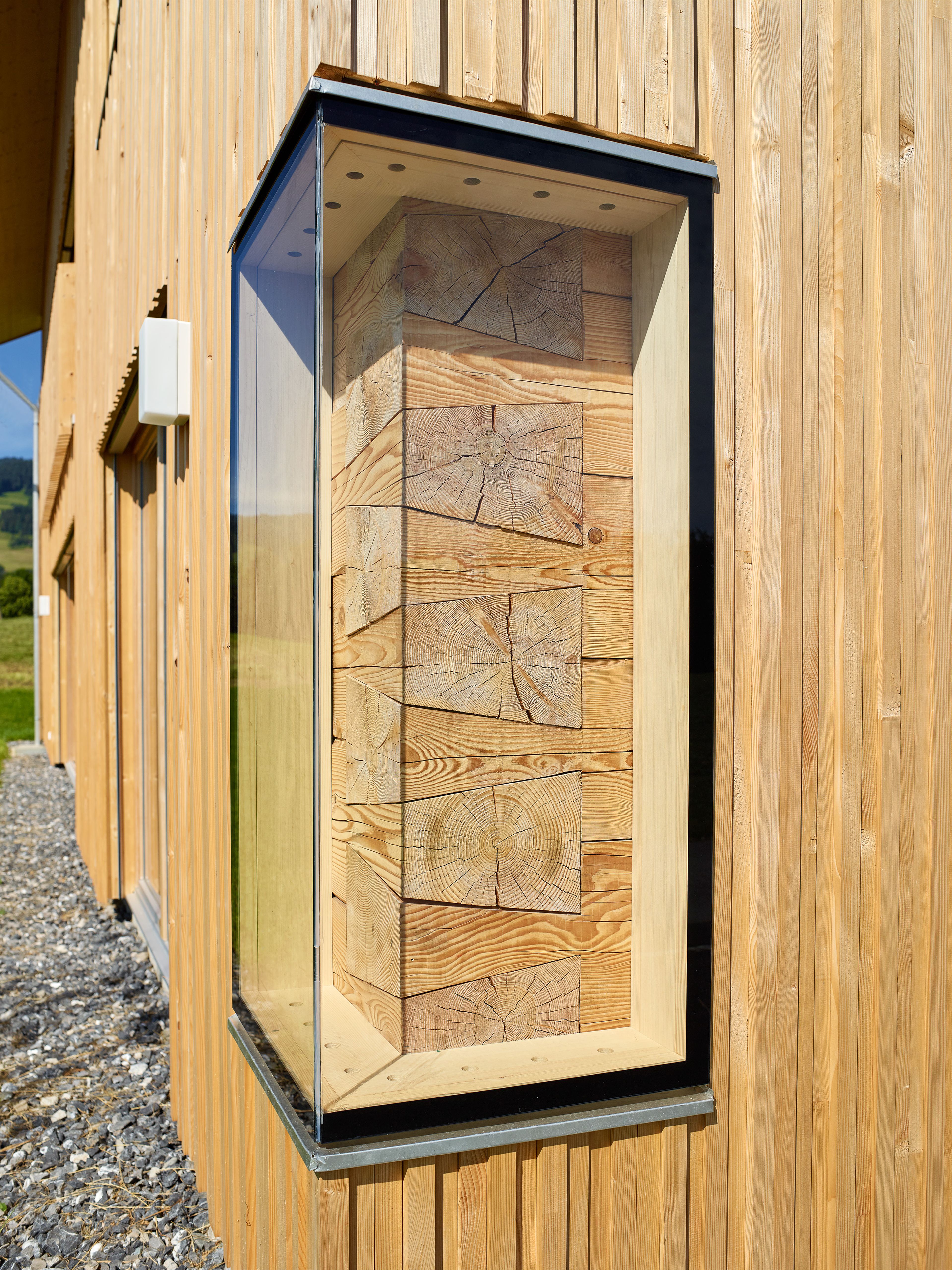 Ein einzigartiges Wertvollholzhaus aus massiven Holzbalken in traditioneller Strickbauweise, eingebettet in eine üppig grüne Landschaft unter offenem Himmel.