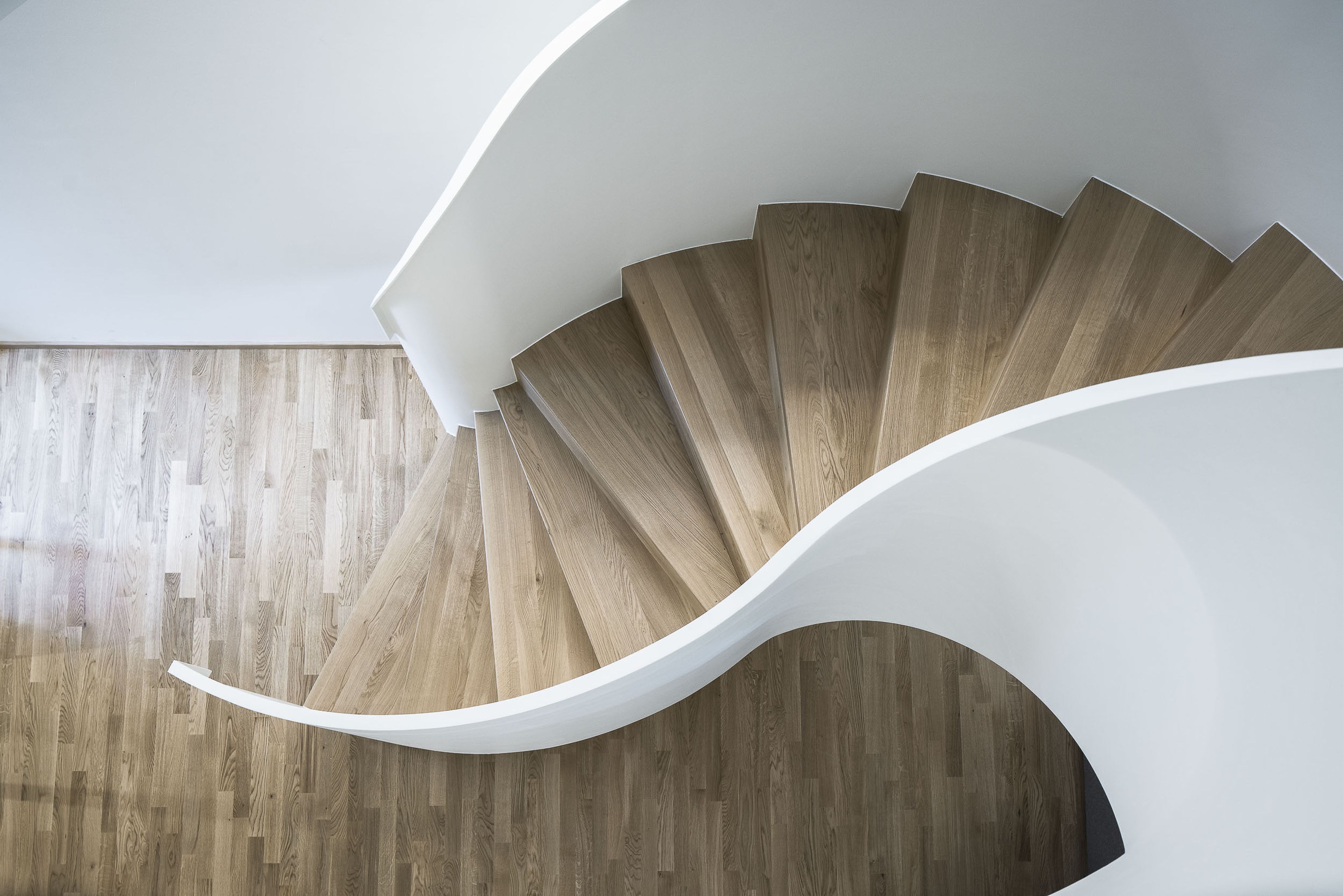Eine hölzerne Wendeltreppe mit elegantem, weißem Geländer, von oben betrachtet, bildet einen Kontrast zum passenden Holzboden.