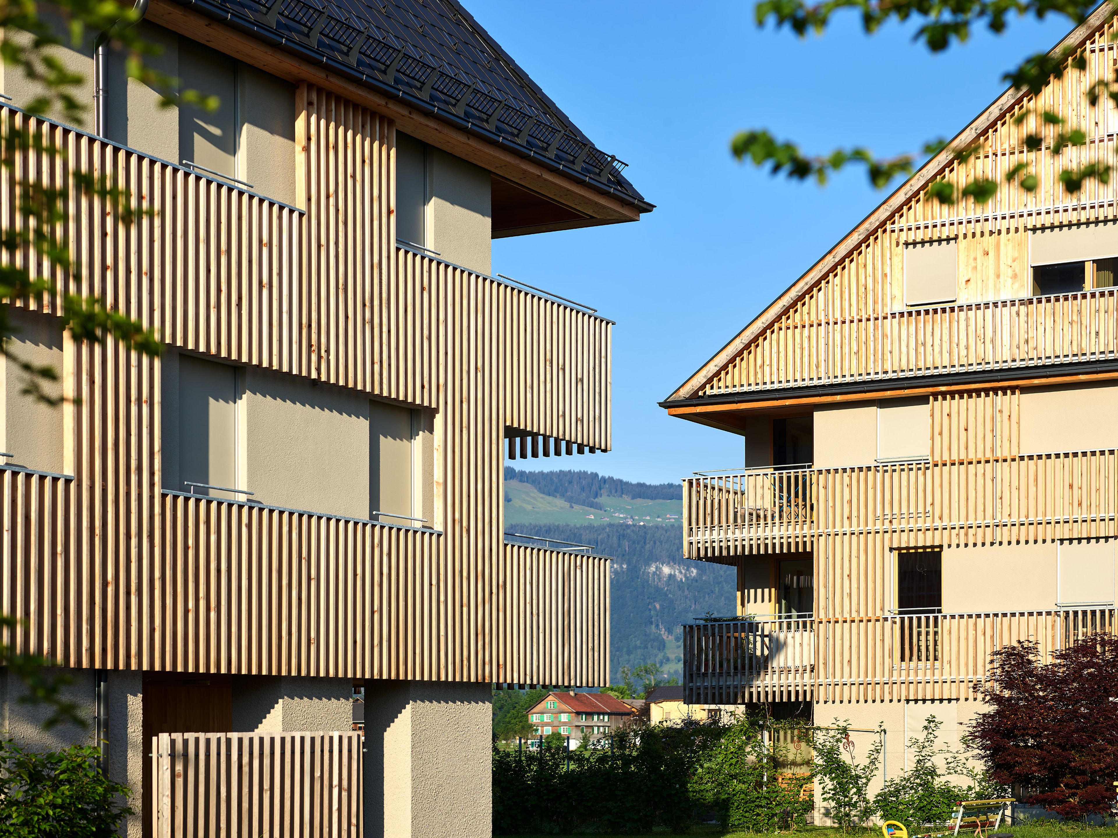 Wohnanlage in Holzbauweise mit moderner Architektur und Holzfassade und Satteldach; rund um das Gebäude erstreckt sich viel Grünfläche.