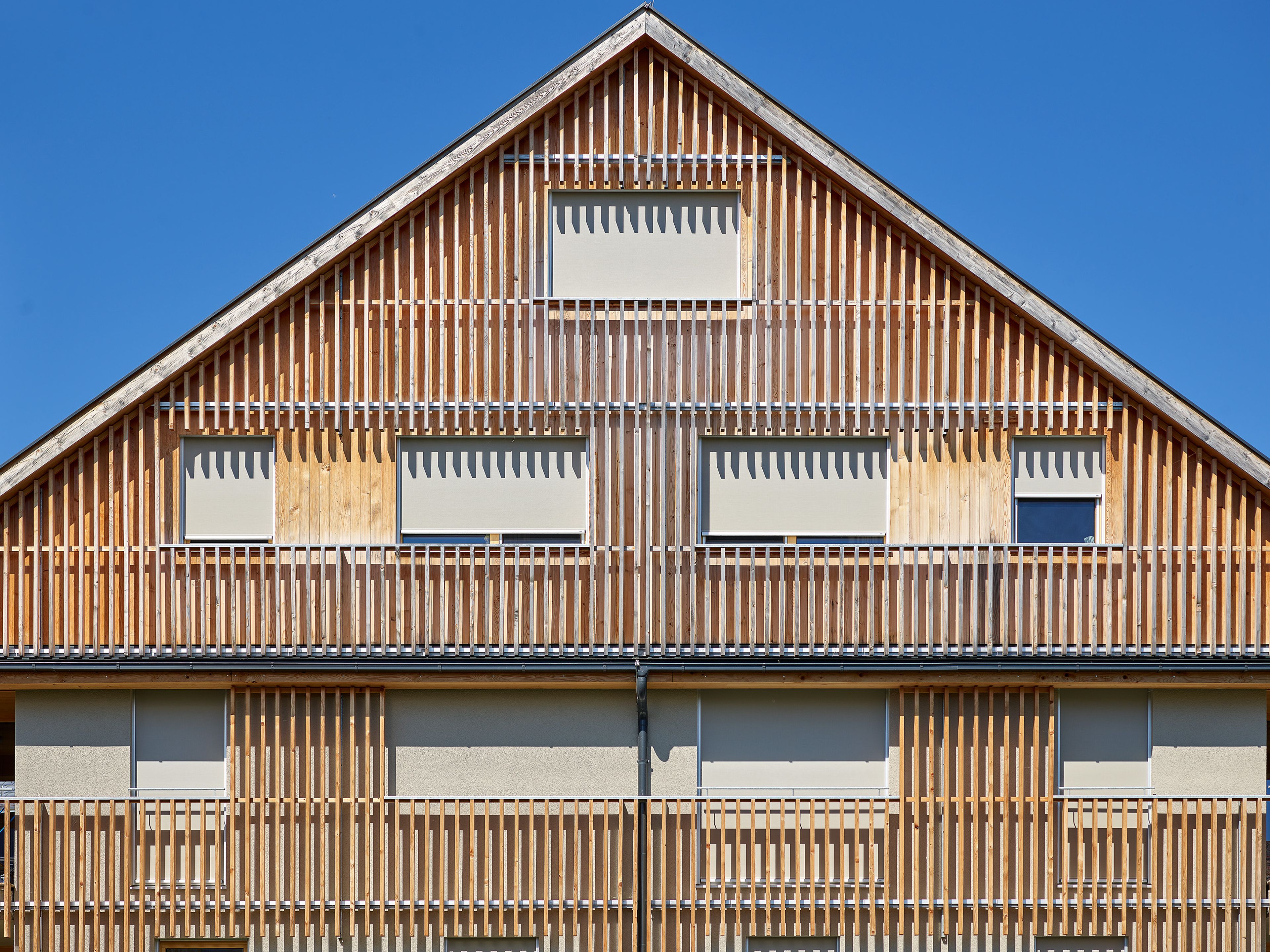 Wohnanlage in Holzbauweise mit moderner Architektur und Holzfassade und Satteldach; rund um das Gebäude erstreckt sich viel Grünfläche.