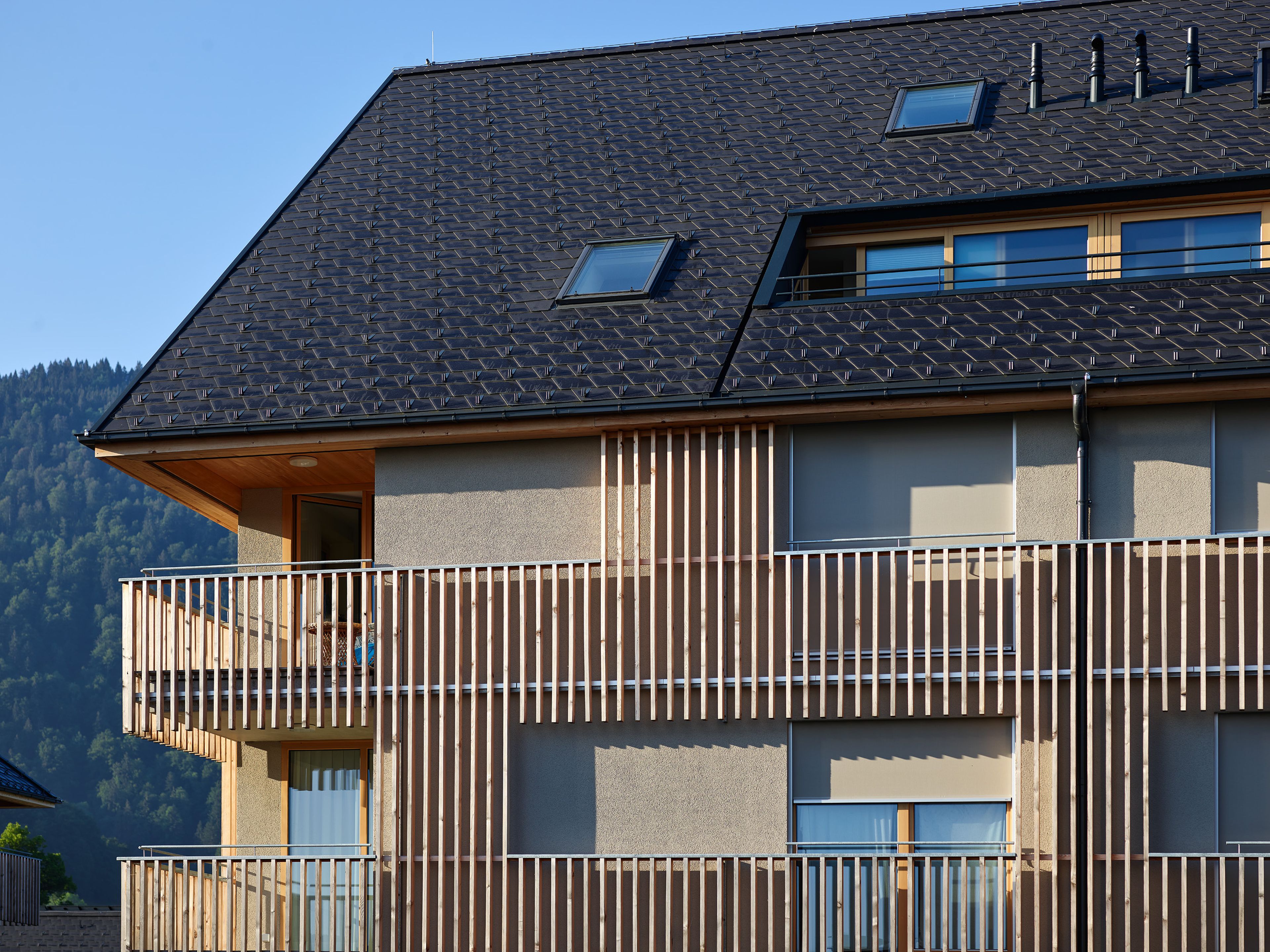 Wohnanlage in Holzbauweise mit moderner Architektur und Holzfassade und Satteldach; rund um das Gebäude erstreckt sich viel Grünfläche.