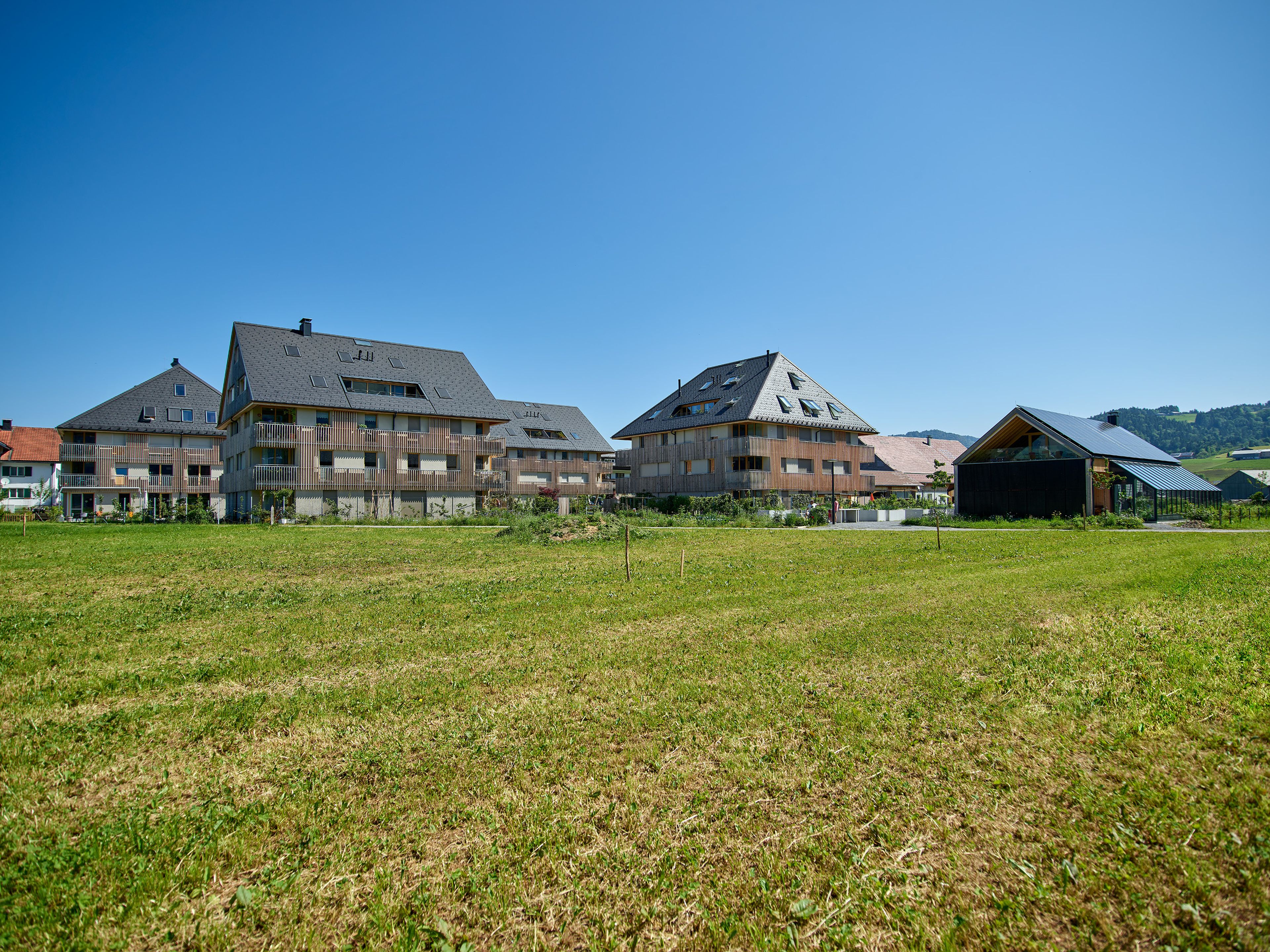 Wohnanlage in Holzbauweise mit moderner Architektur und Holzfassade und Satteldach; rund um das Gebäude erstreckt sich viel Grünfläche.