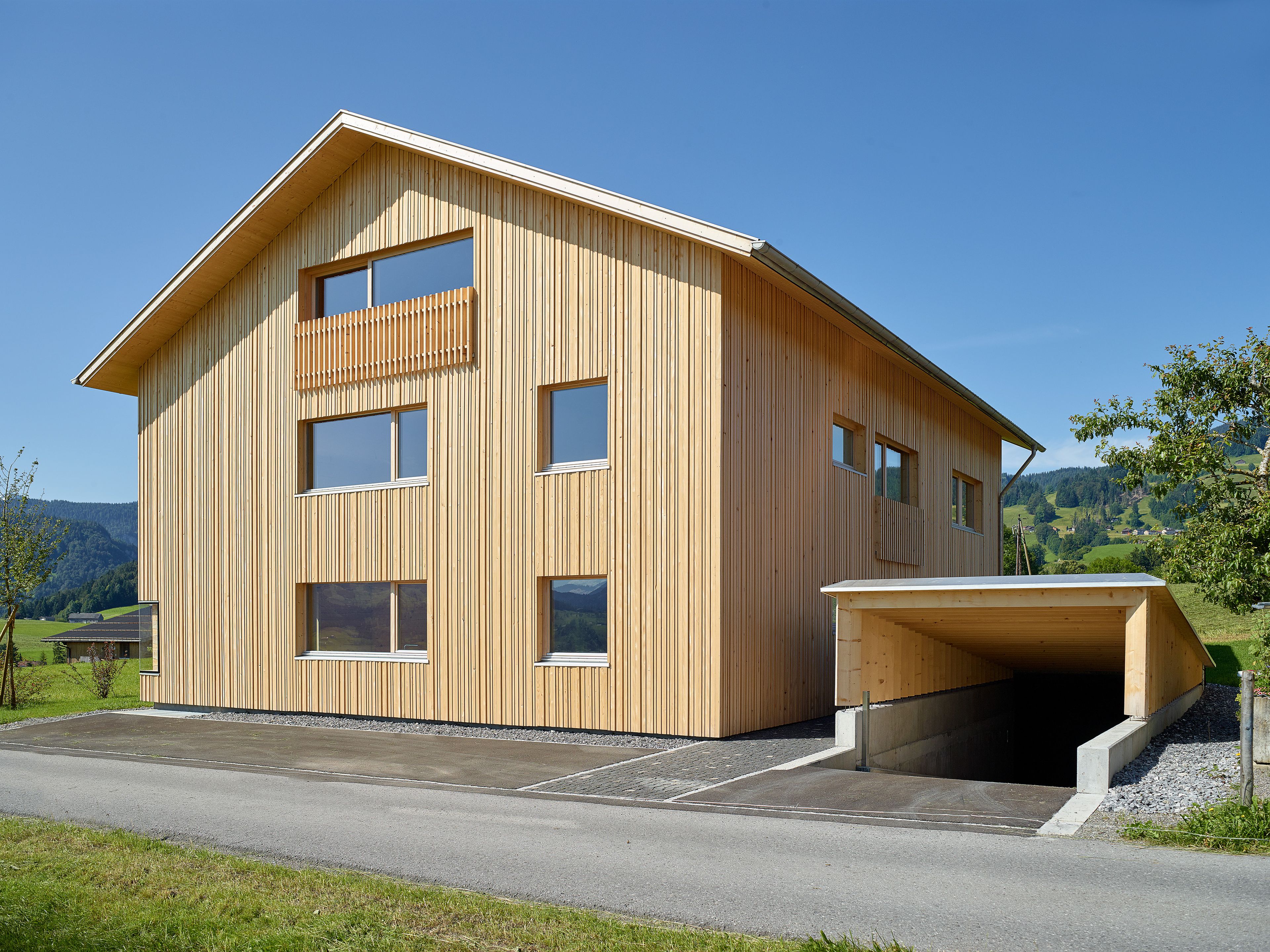 Ein einzigartiges Wertvollholzhaus aus massiven Holzbalken in traditioneller Strickbauweise, eingebettet in eine üppig grüne Landschaft unter offenem Himmel.
