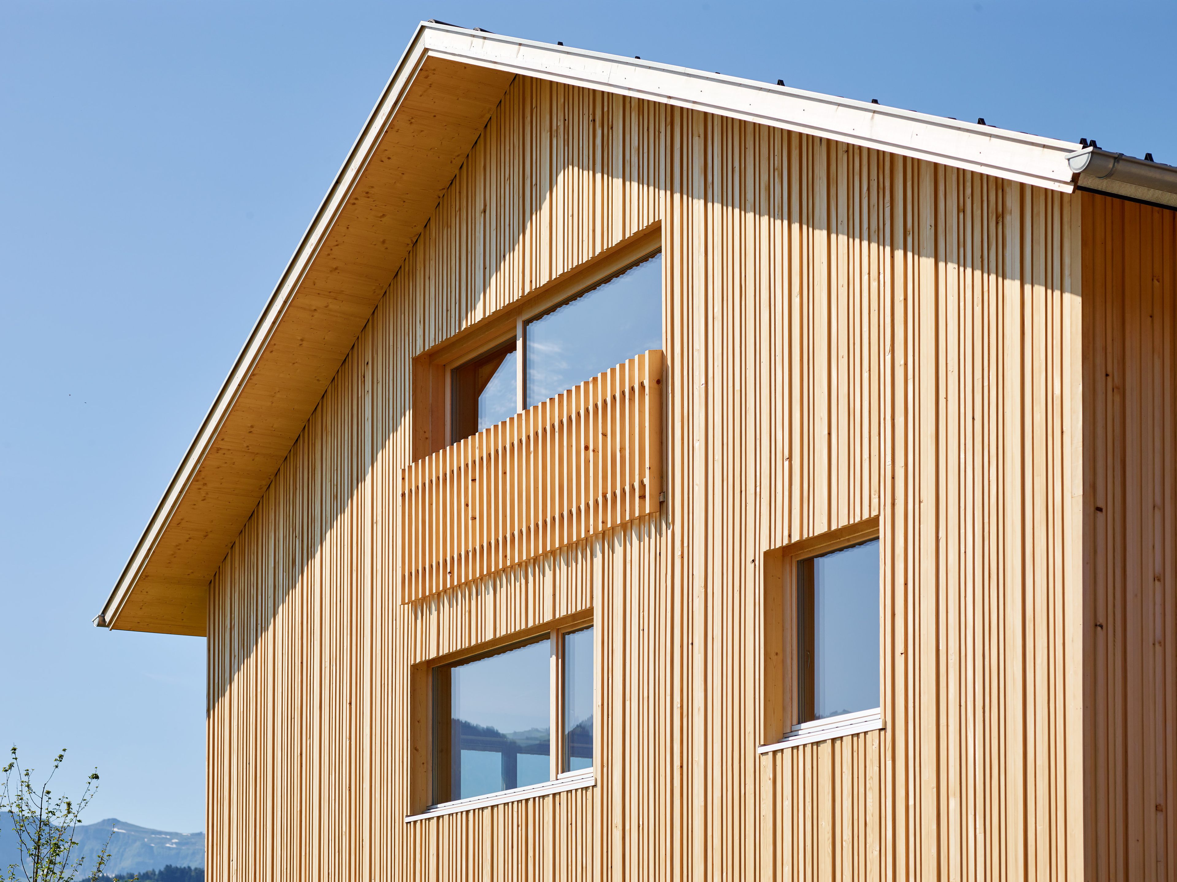 Ein einzigartiges Wertvollholzhaus aus massiven Holzbalken in traditioneller Strickbauweise, eingebettet in eine üppig grüne Landschaft unter offenem Himmel.