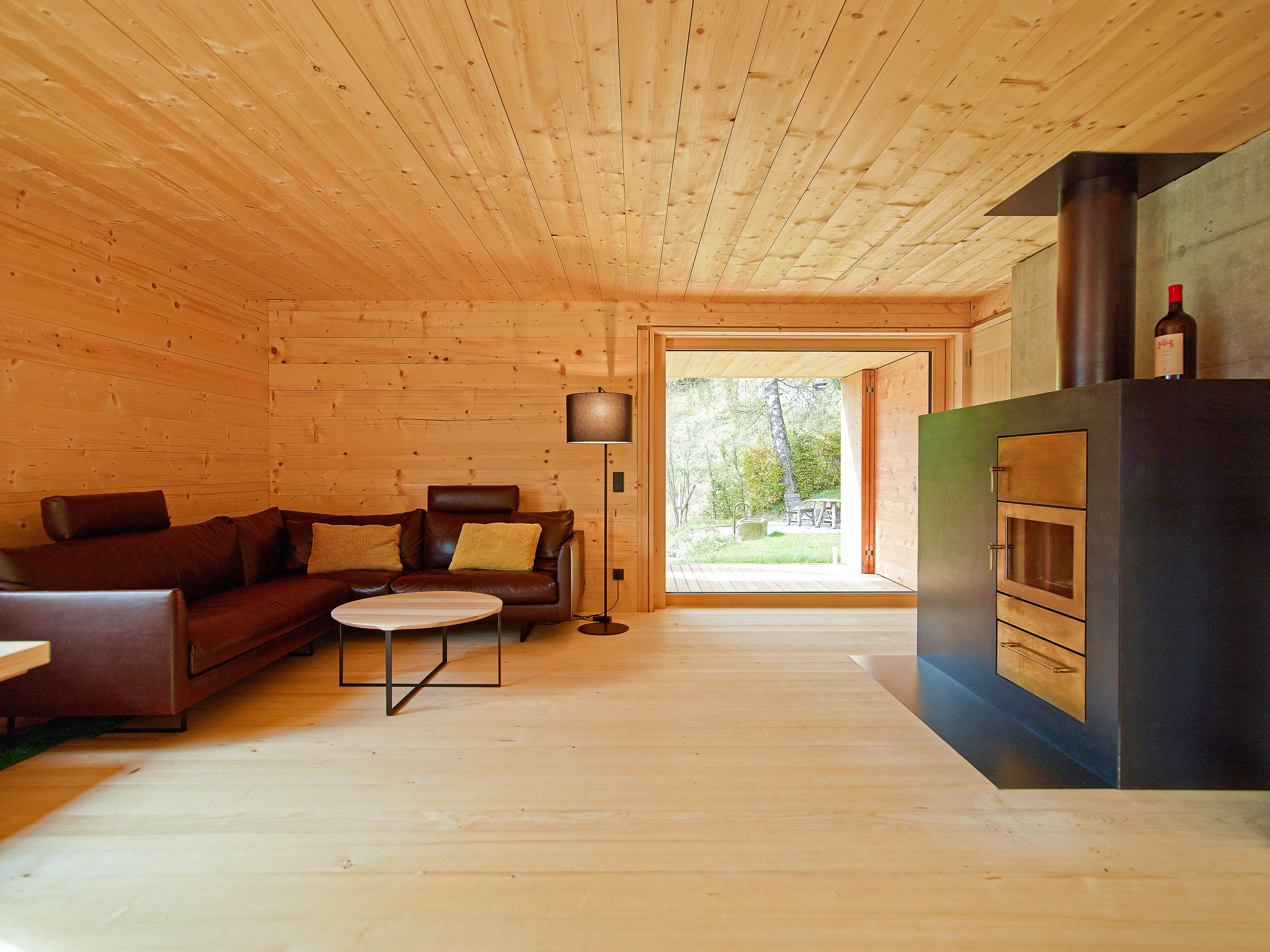 Innenaufnahme eines Einfamilienhauses in Holz – in Strickbauweise. Gemütlicher Raum mit Holzdecke, Holzboden und Kaminofen.