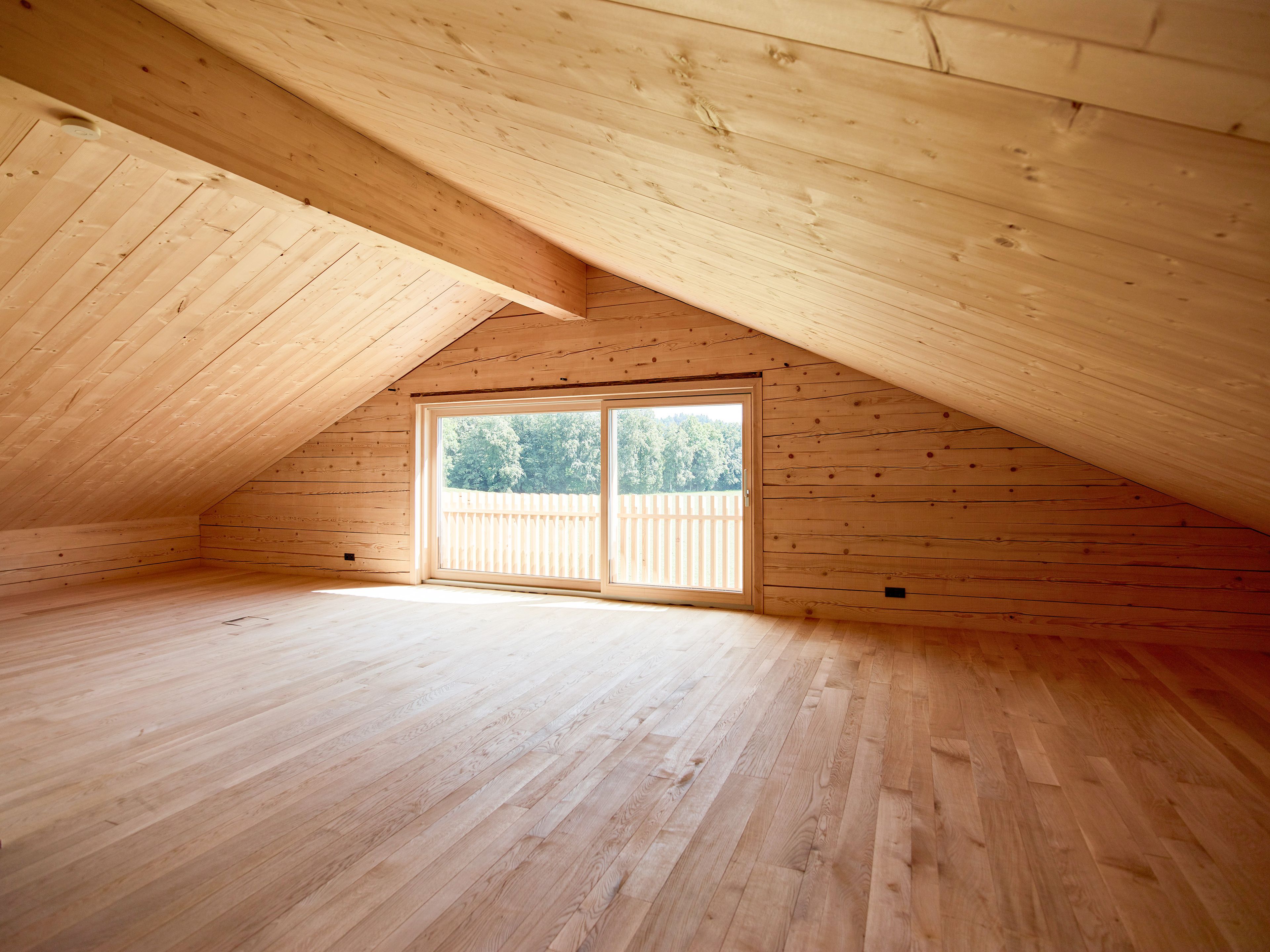 Innenansicht Dachausbau eines Wertvollholzhauses mit sichtbaren massiven Holzbalken, warmem Holzton und gemütlicher, natürlicher Atmosphäre.