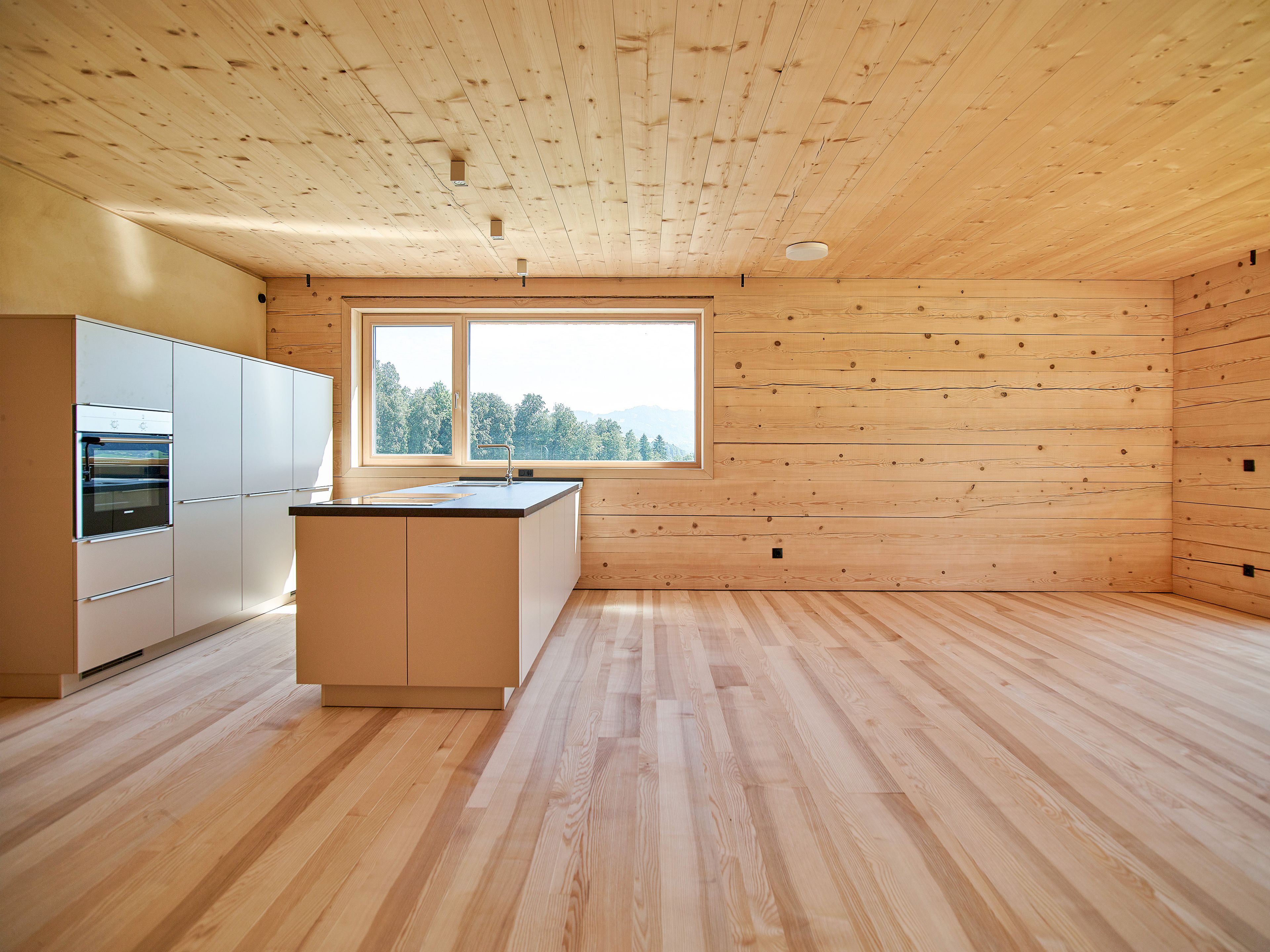 Innenansicht mit Küche eines Wertvollholzhauses mit sichtbaren massiven Holzbalken, warmem Holzton und gemütlicher, natürlicher Atmosphäre.