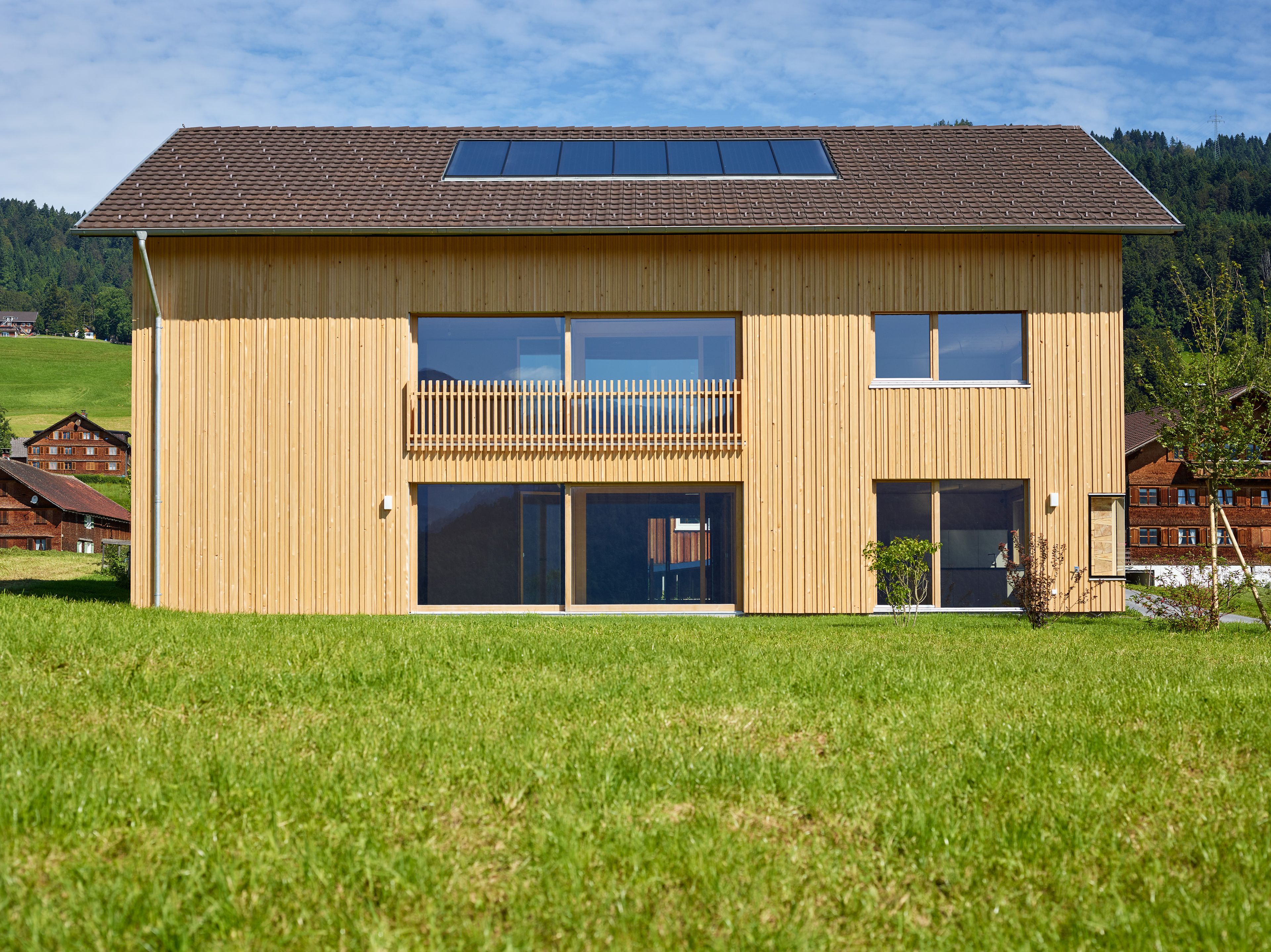 Ein einzigartiges Wertvollholzhaus aus massiven Holzbalken in traditioneller Strickbauweise, eingebettet in eine üppig grüne Landschaft unter offenem Himmel.