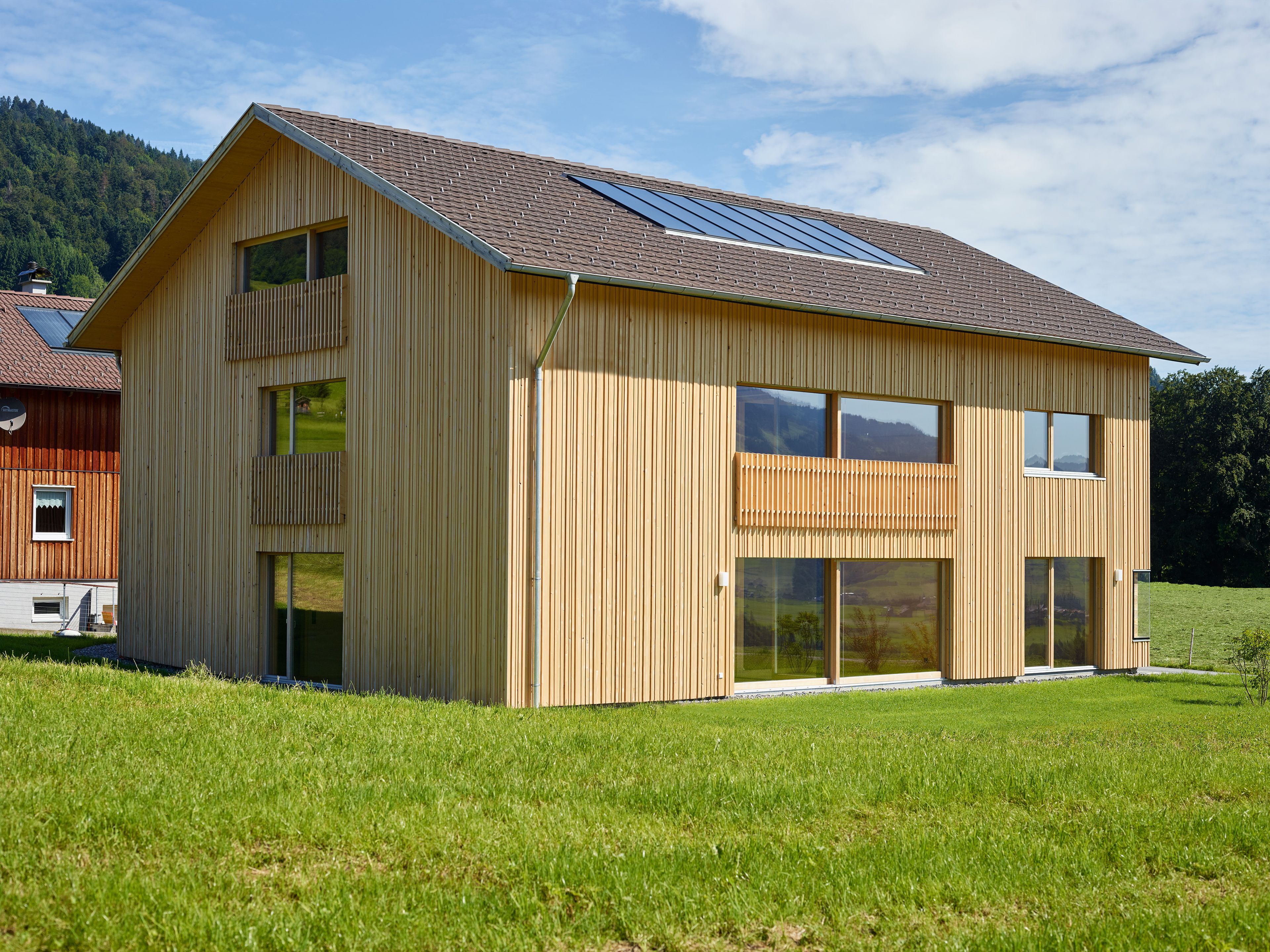 Ein einzigartiges Wertvollholzhaus aus massiven Holzbalken in traditioneller Strickbauweise, eingebettet in eine üppig grüne Landschaft unter offenem Himmel.