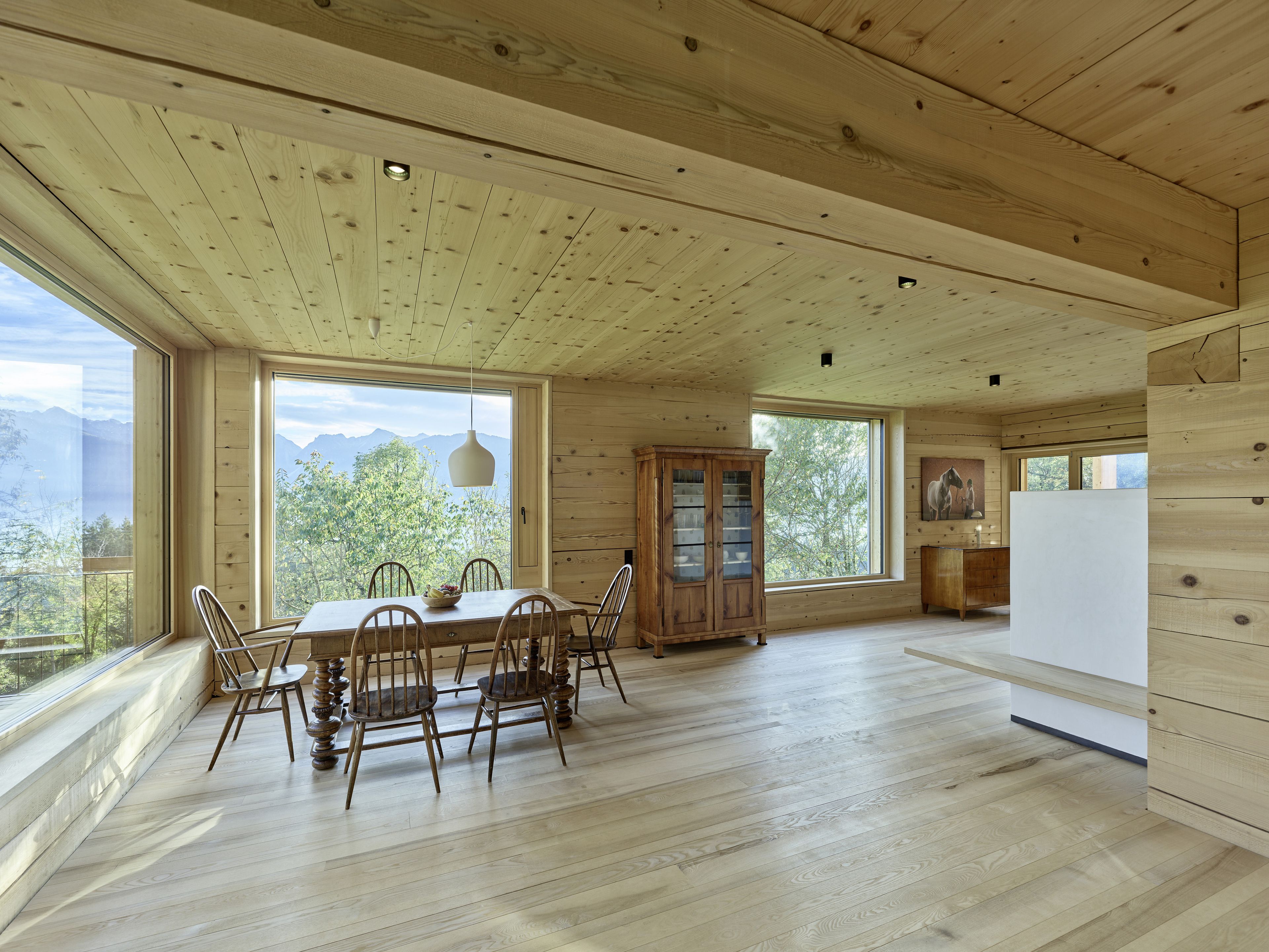Essbereich mit Holzverkleidung, großen Fenstern mit Bergblick, einem Holztisch mit Stühlen und einer Küche mit dunklen Schränken.