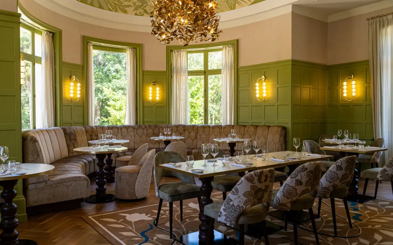 Le restaurant L'Attilio Vertou, aux murs lambrissés de vert, doté de sièges moelleux, de lustres décoratifs et de tables dressées pour le dîner, offrant une atmosphère chaleureuse et accueillante.