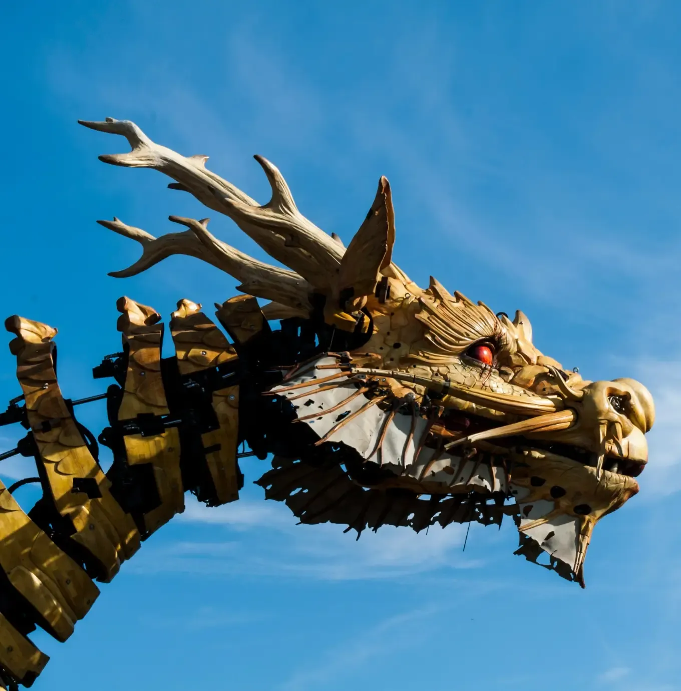 Une tête de dragon mécanique dorée, ornée de bois, se détachant sur un ciel bleu limpide.
