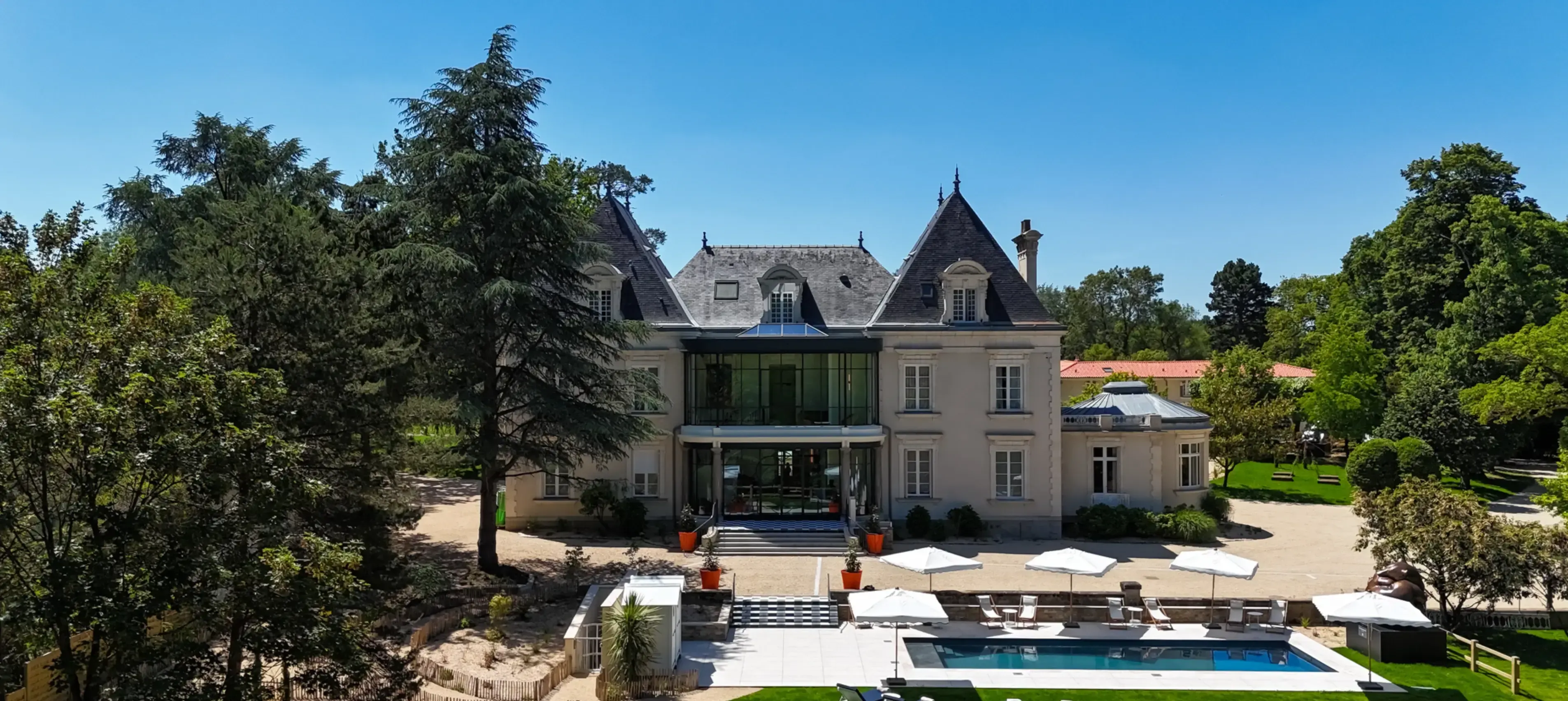 Vu sur le Château du Portereau avec piscine, niché au cœur d'une végétation luxuriante et d'arbres, sous un ciel d'un bleu éclatant.