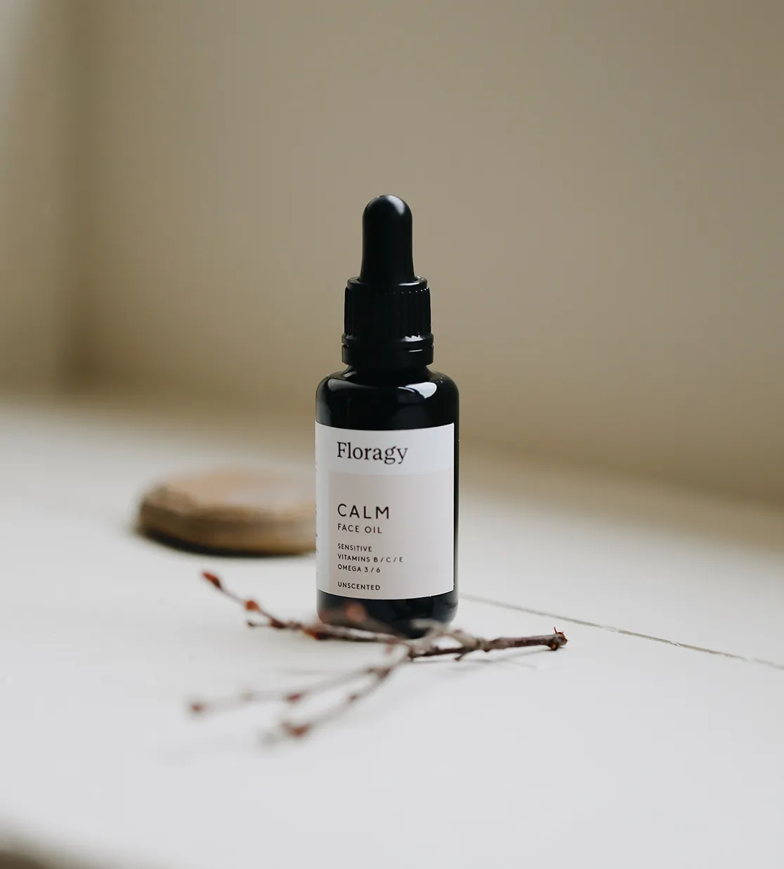 Dark glass dropper bottle labeled Floragy CALM Face Oil on a white surface with a soft beige background.