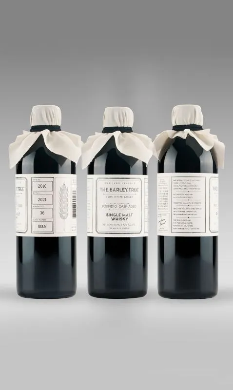 Three miron glass whisky bottles with white fabric caps and parchment-style labels, aligned in a row against a gray gradient background.