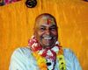 Advaita Master H.W.L. Poonja (Papaji), the Guru of Madhukar, smiling brightly in a festive Indian setting, wearing a flower garland.