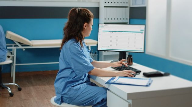 Woman working as nurse with computer and documents in cabinet, checking files for examination appointment. Medical assistant looking at screen for patient information and checkup visit