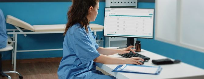Woman working as nurse with computer and documents in cabinet, checking files for examination appointment. Medical assistant looking at screen for patient information and checkup visit