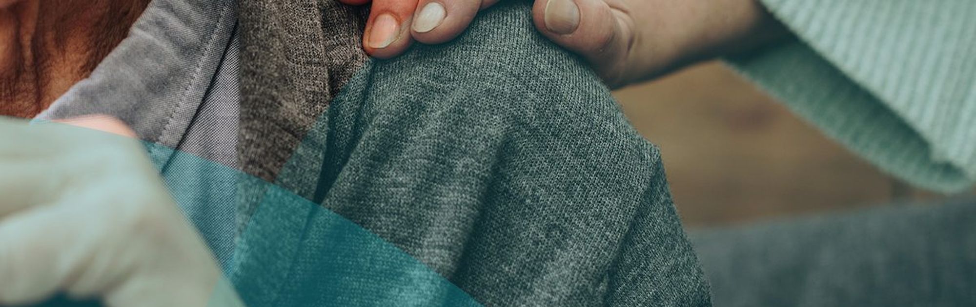 Elderly person in a grey sweater with a hand resting on their shoulder, showing comfort and support.