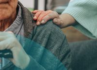 Elderly person in a grey sweater with a hand resting on their shoulder, showing comfort and support.