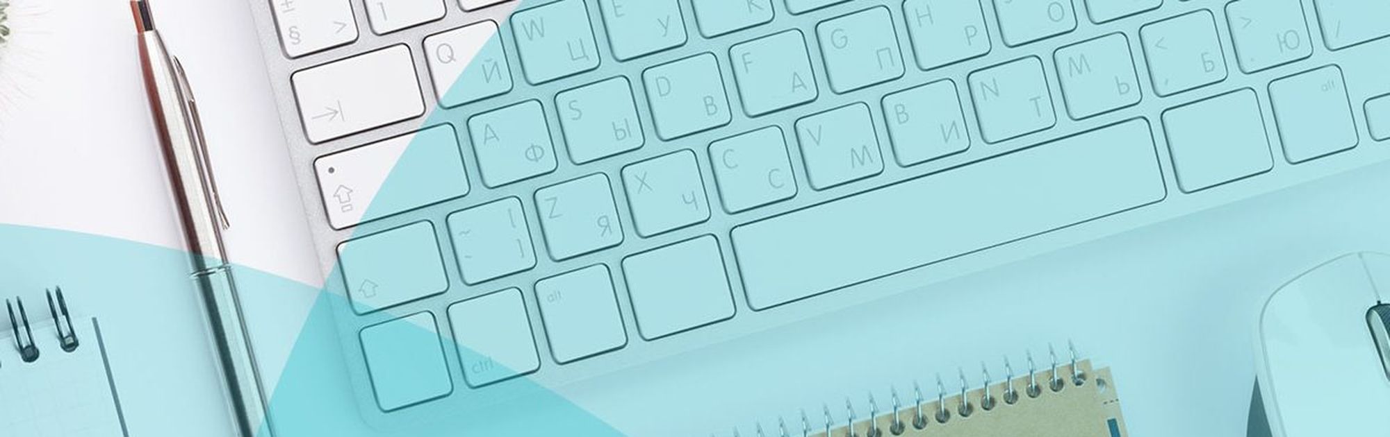A desk setup with a keyboard, glasses, pen, notepad, and a mouse on a light blue surface.