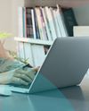 Person typing on a laptop at a desk, with books and plant in the background. Office setting.