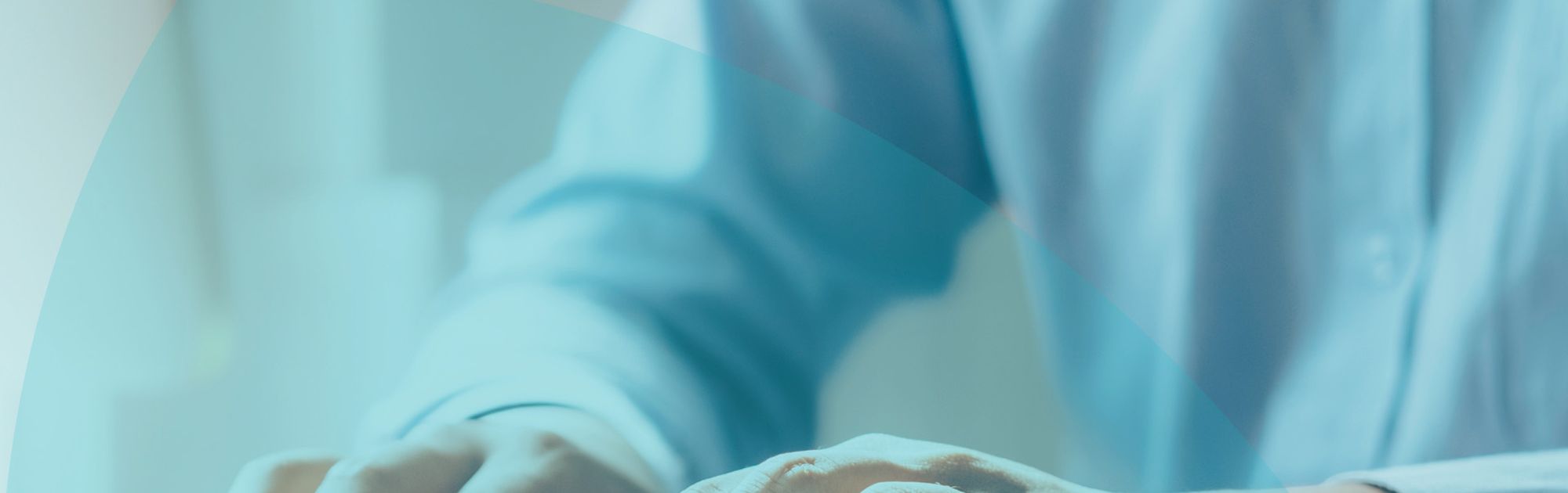 Person in a blue shirt typing on a keyboard at a desk, with soft lighting and a blurred background.