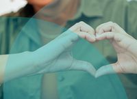 Person in a green shirt forming a heart shape with their hands, smiling softly, with an abstract blue overlay.