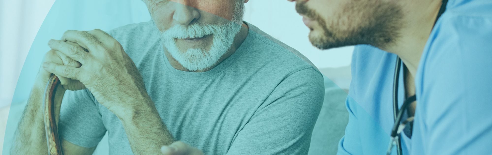 Elderly man with cane and younger doctor in scrubs discuss information on a tablet in a well-lit room.