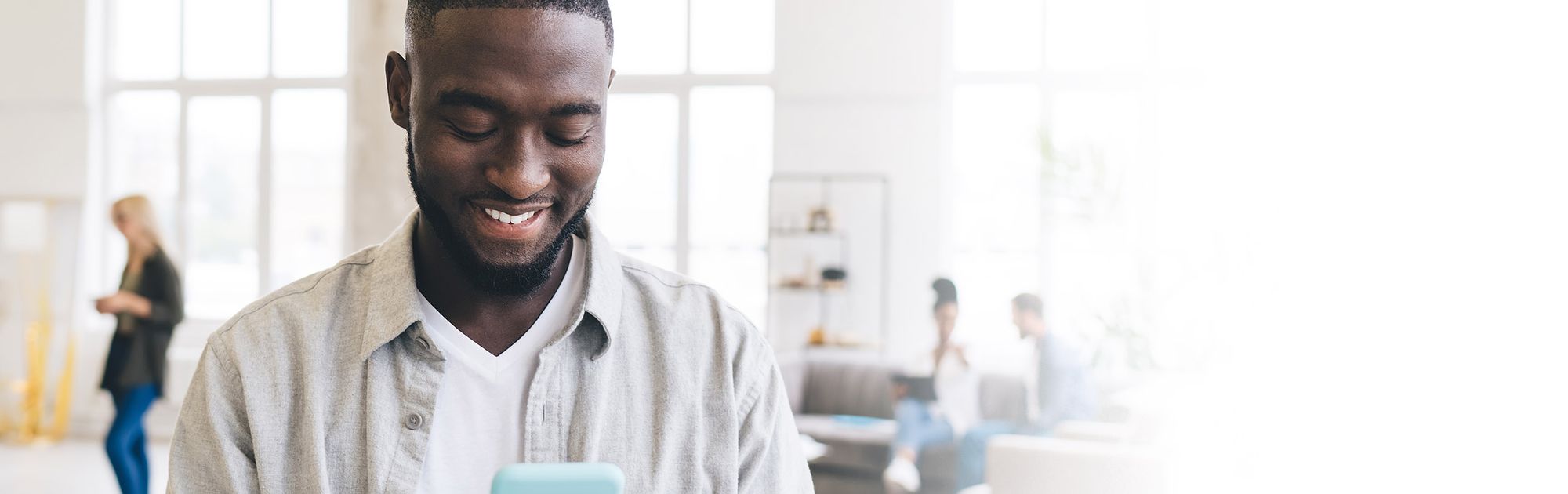 A smiling man uses a smartphone in a bright, modern office.
