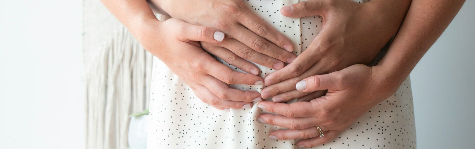 Close-up of a couple embracing with hands on a woman's belly, both wearing speckled clothing, symbolizing affection and togetherness.