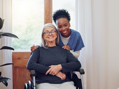 A woman in a wheelchair smiles alongside a caregiver.
