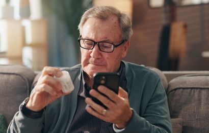 Elderly man on a couch examines a pill bottle.