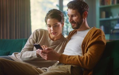 A couple sitting on a couch looks at a smartphone together.