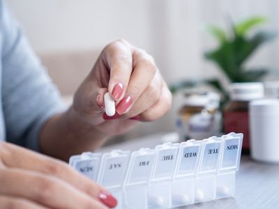 Person placing a white pill into a labeled pill organizer.