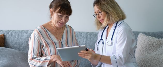 Doctor in a white coat shows a tablet to an older woman.