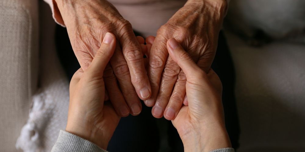 A young person is holding the hands of an elderly lady.