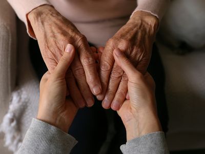 A young person is holding the hands of an elderly lady.