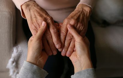 A young person is holding the hands of an elderly lady.
