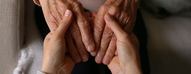 A young person is holding the hands of an elderly lady.