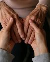Two pairs of hands: younger hands gently holding and comforting older hands, conveying care and connection.