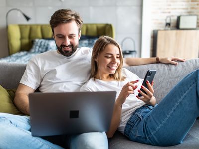 A man uses a laptop and a woman smiles at her smartphone.